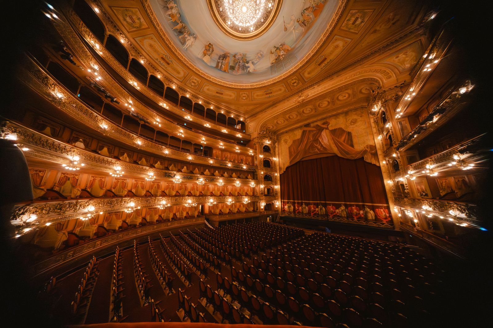 Interior de una sala de ópera con butacas rojas y escenario iluminado.