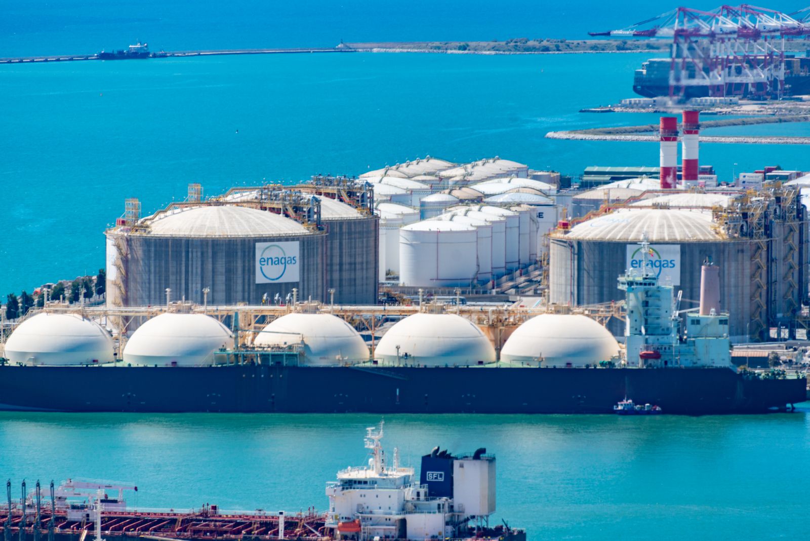 Planta de gas natural licuado junto al mar con tanques de almacenamiento y tuberías industriales.