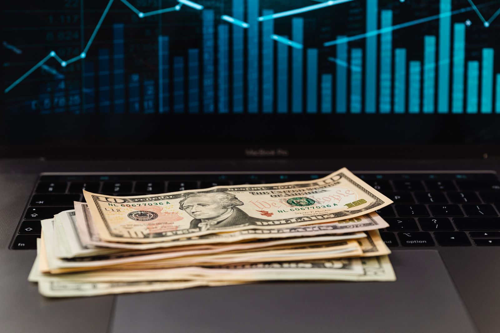 Billetes de dólar y monedas latinoamericanas sobre un escritorio con gráficos financieros de fondo